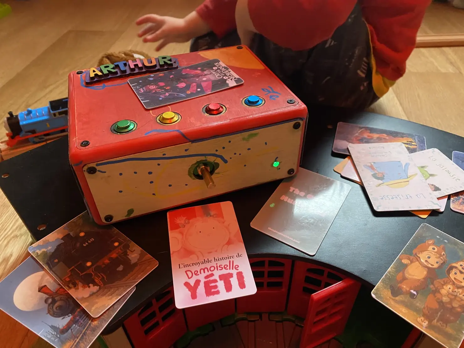 Le prototype fait pour mon fils : structure imprimée en 3D, faces en plaques de bois qu'on a peintes ensemble, et son prénom assemblé avec des lettres découpées au laser collées sur le dessus. Il manque encore le cache du bouton de volume.